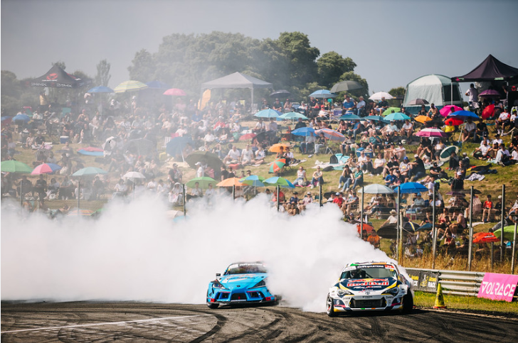 Two cars in a tsuiso battle wrapped in smoke in front of a huge crowd